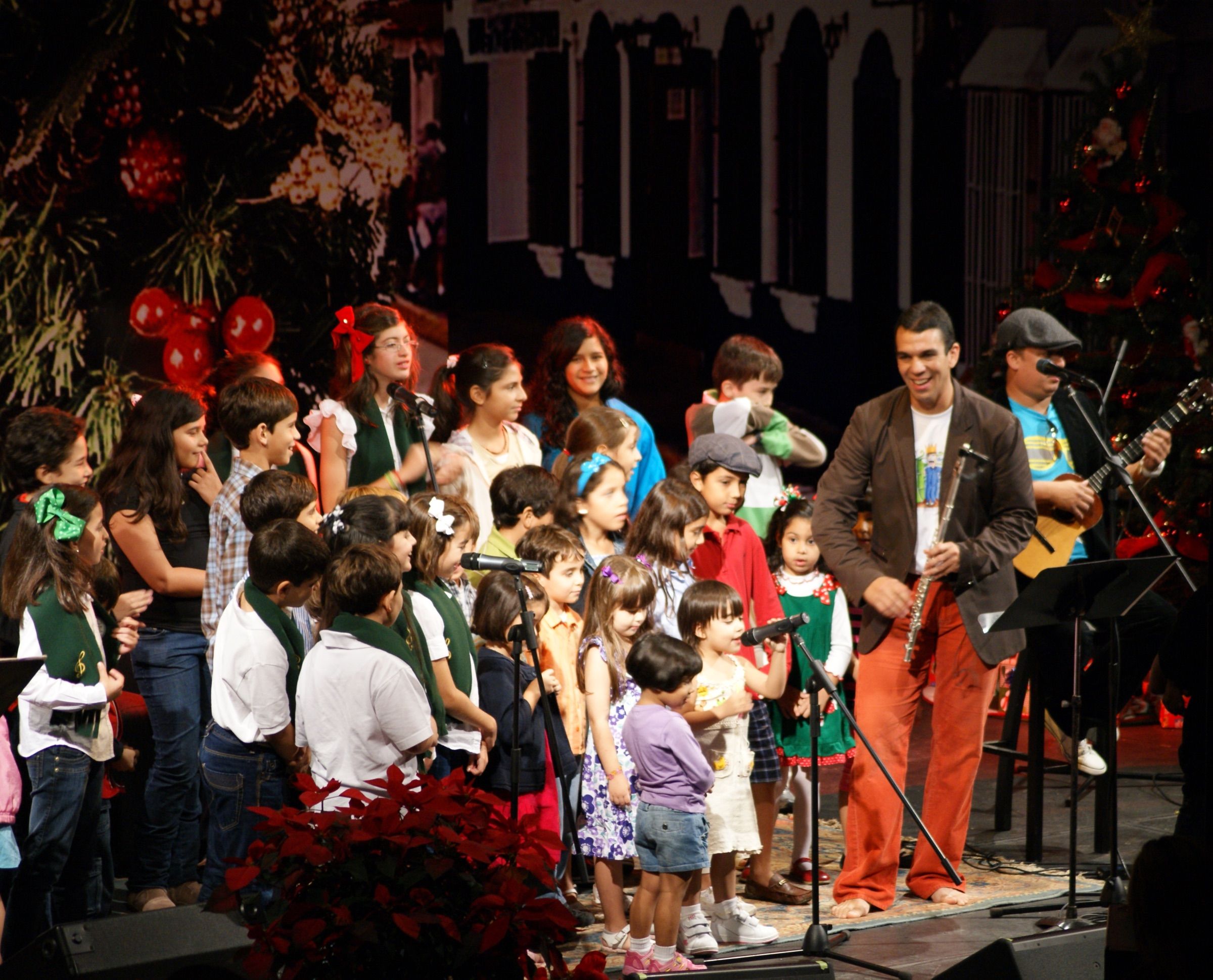 Huáscar Barradas con su flauta junto a un coro de niños en un escenario decorado de navidad.