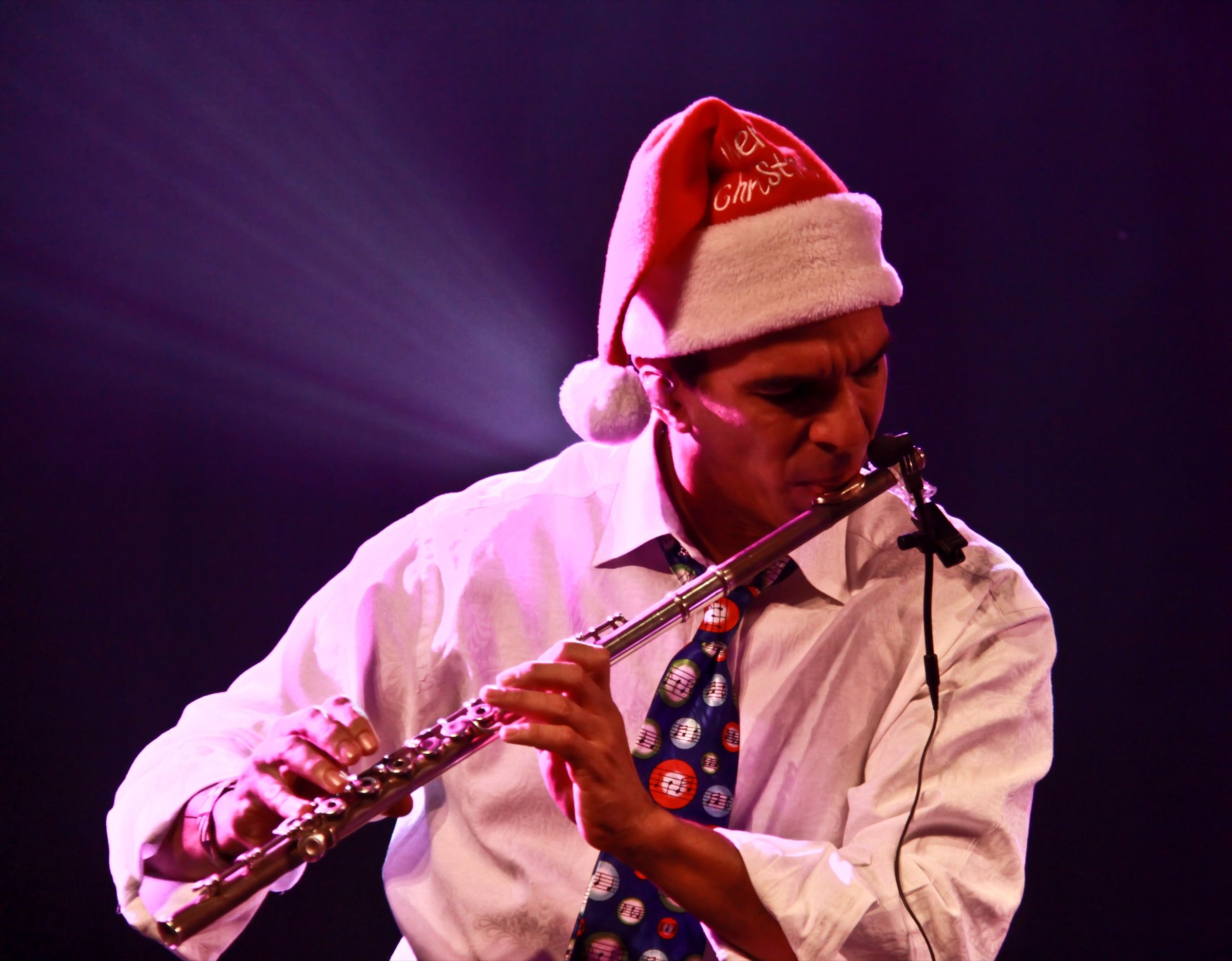 Huáscar Barradas tocando la flauta con un gorro de navidad, bajo una luz violeta.