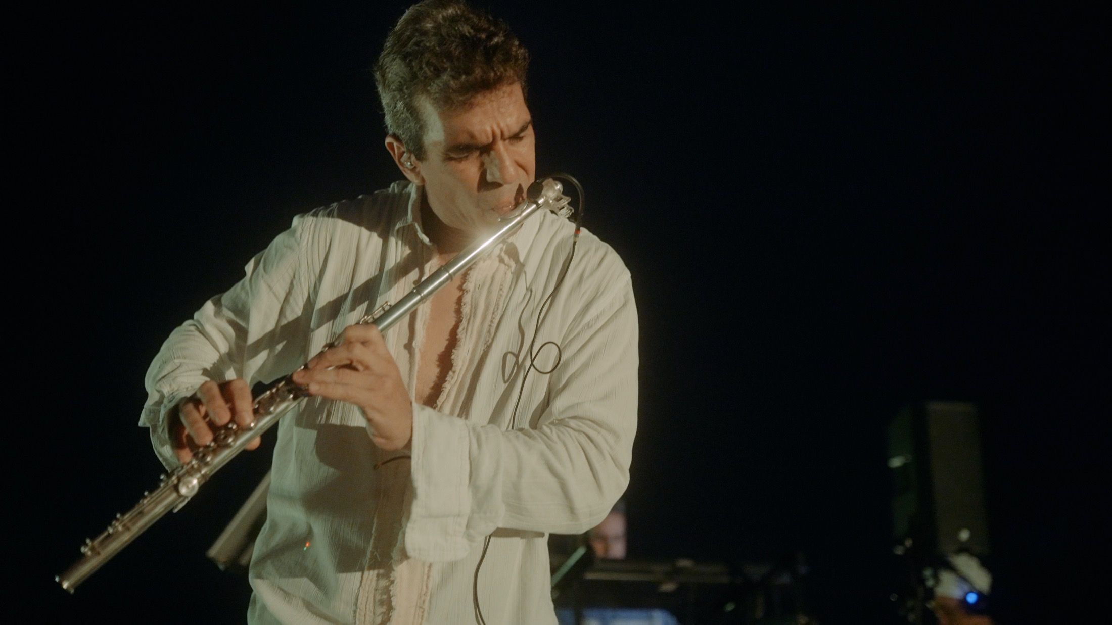 Huáscar Barradas tocando la flauta en concierto, iluminado sobre un escenario a oscuras.