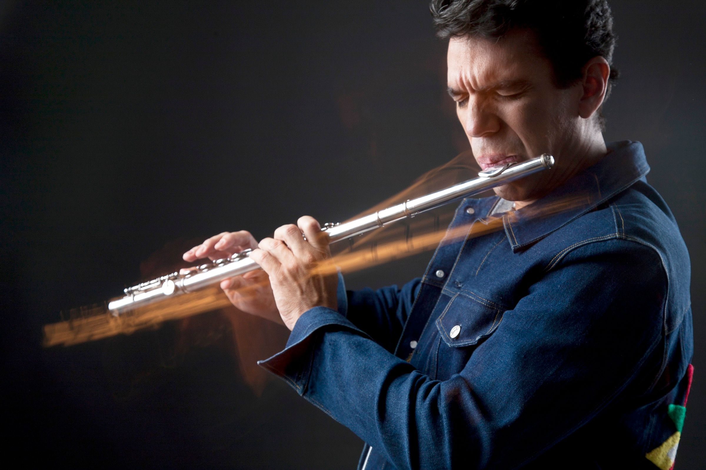 Huáscar Barradas tocando la flauta en estudio, con estelas de luz cálida cruzando el encuadre.