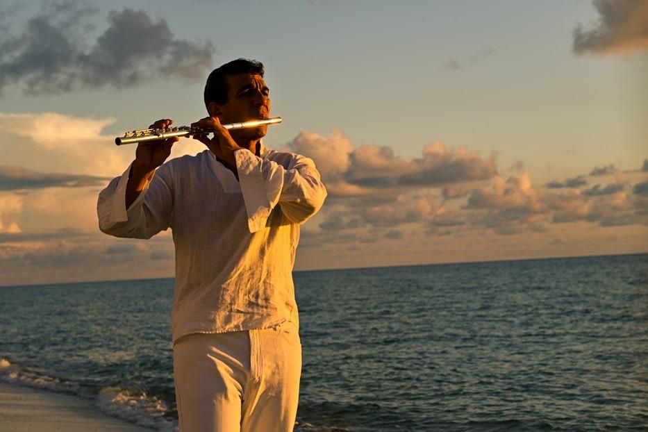 Huáscar Barradas tocando la flauta en la orilla del mar, al atardecer.
