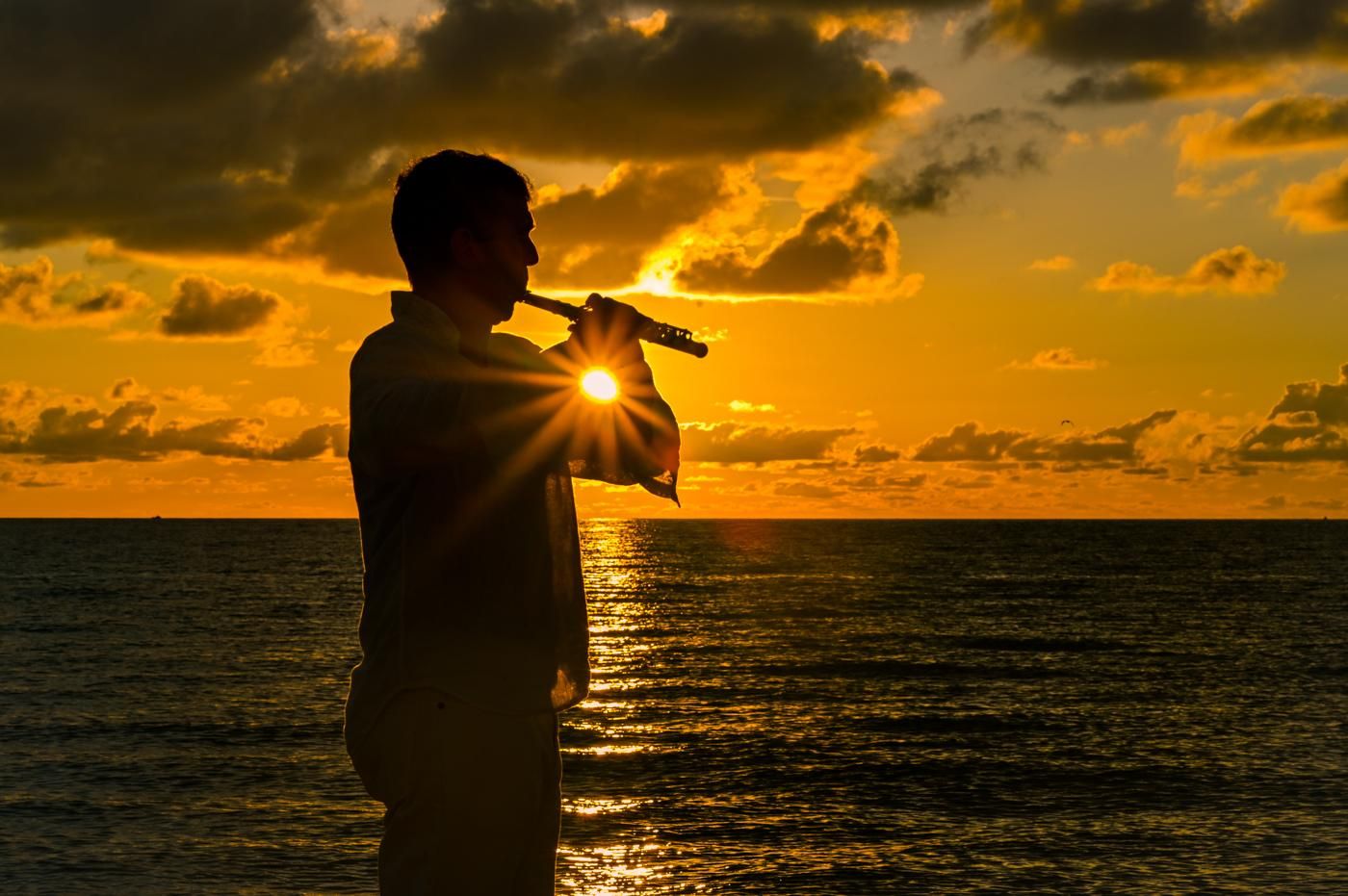Huáscar Barradas tocando la flauta a contraluz, recortado contra un atardecer sobre el mar.